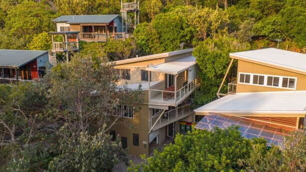 Une maison à plusieurs étages dotée d’un balcon, entourée d’une végétation luxuriante.