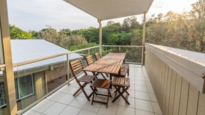 Un balcon abrité, doté d’une table et de chaises en bois, offrant une vue sur la verdure et les bâtiments environnants.