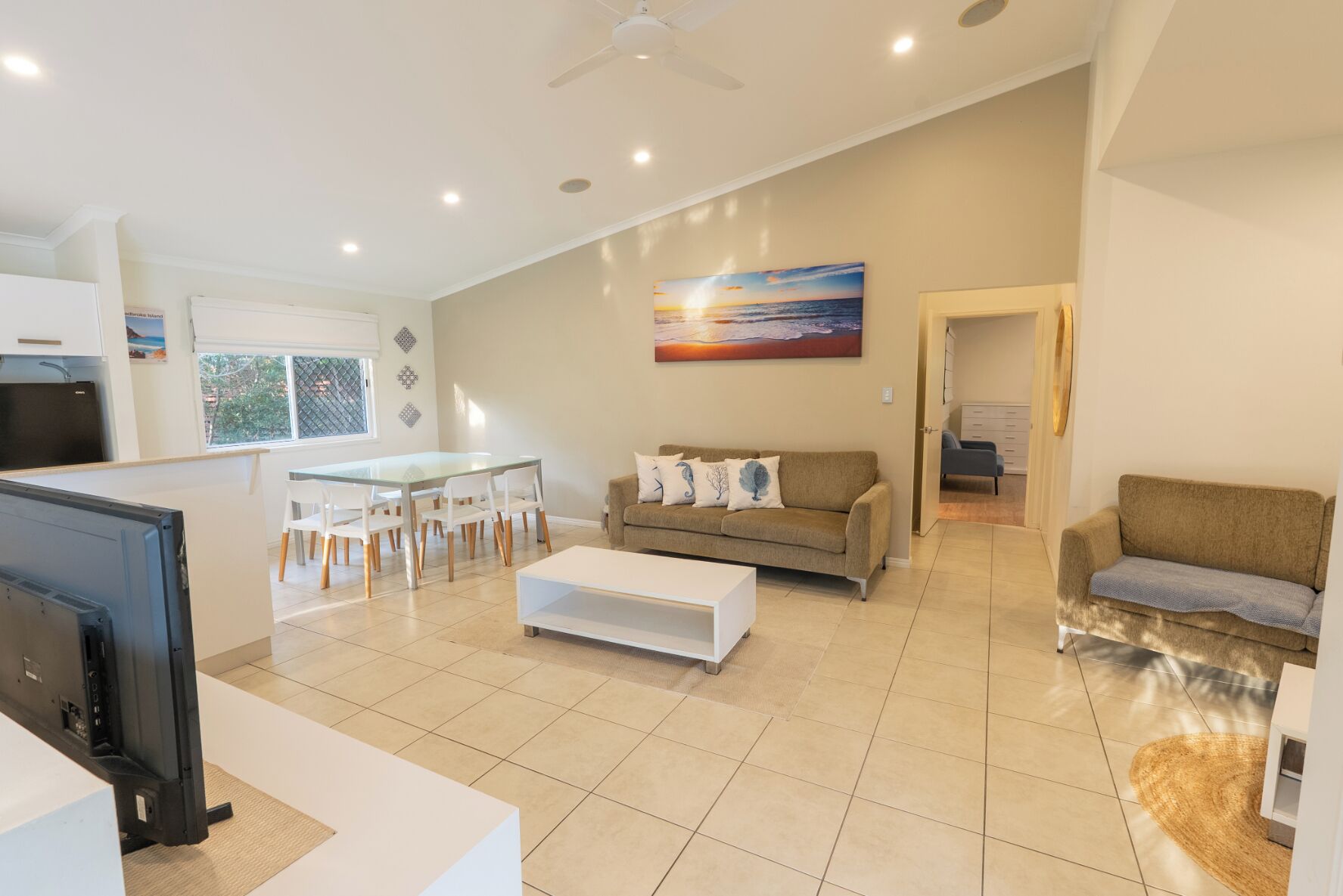 A modern living room with a glass dining table, a sofa, and a TV.