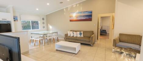 A modern living room with a glass dining table, a sofa, and a TV.
