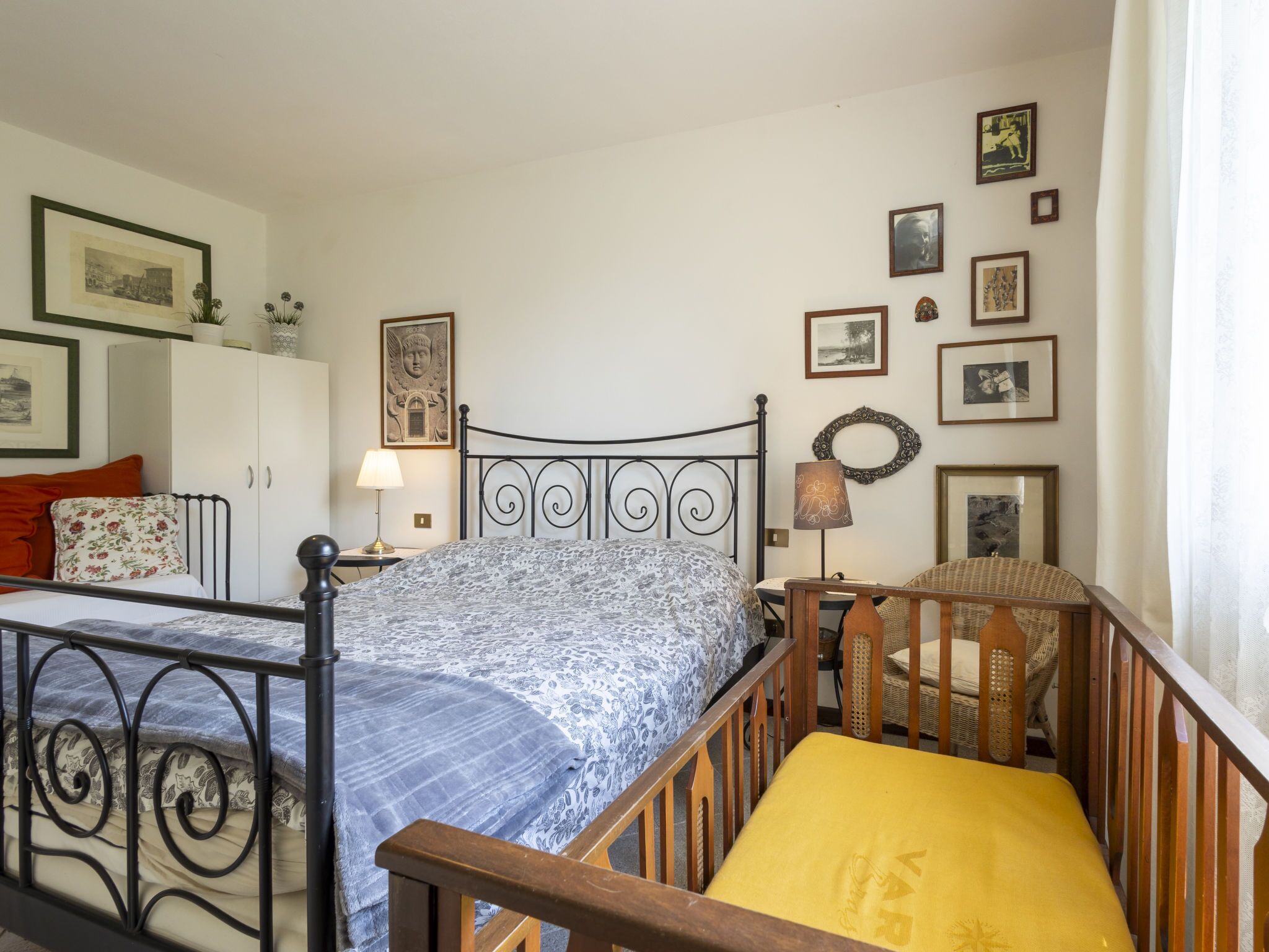 Un dormitorio con una cama, una cuna, un armario y cuadros en la pared.