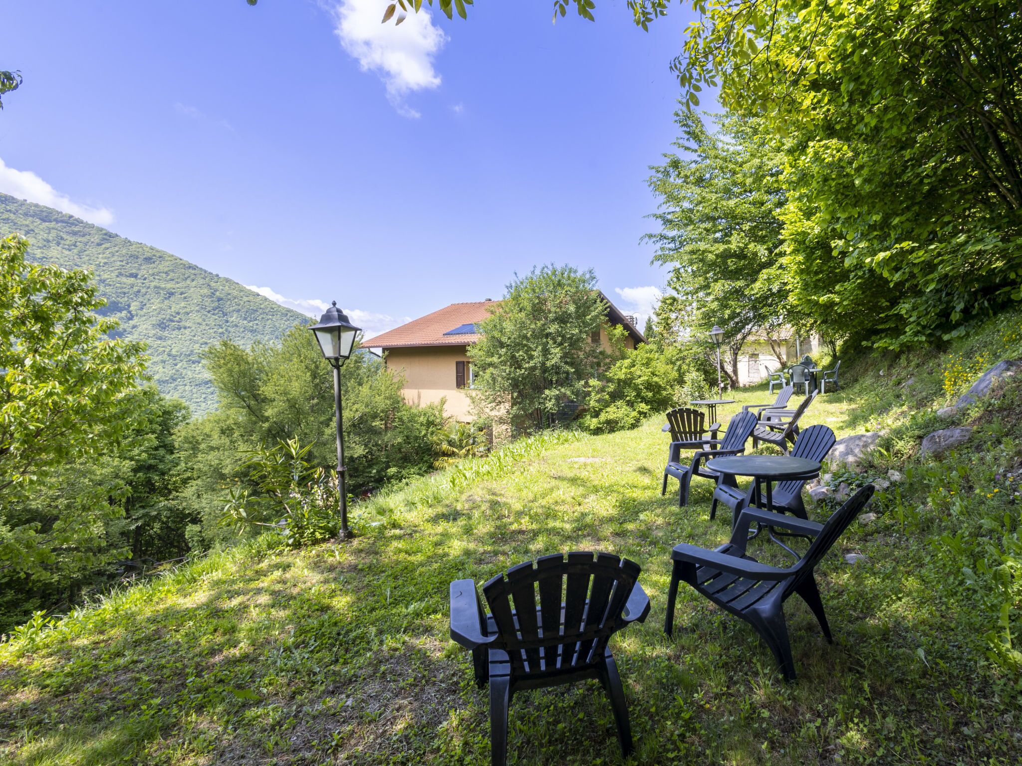 An outdoor seating area with chairs and tables, surrounded by lush greenery and a mountain backdrop.