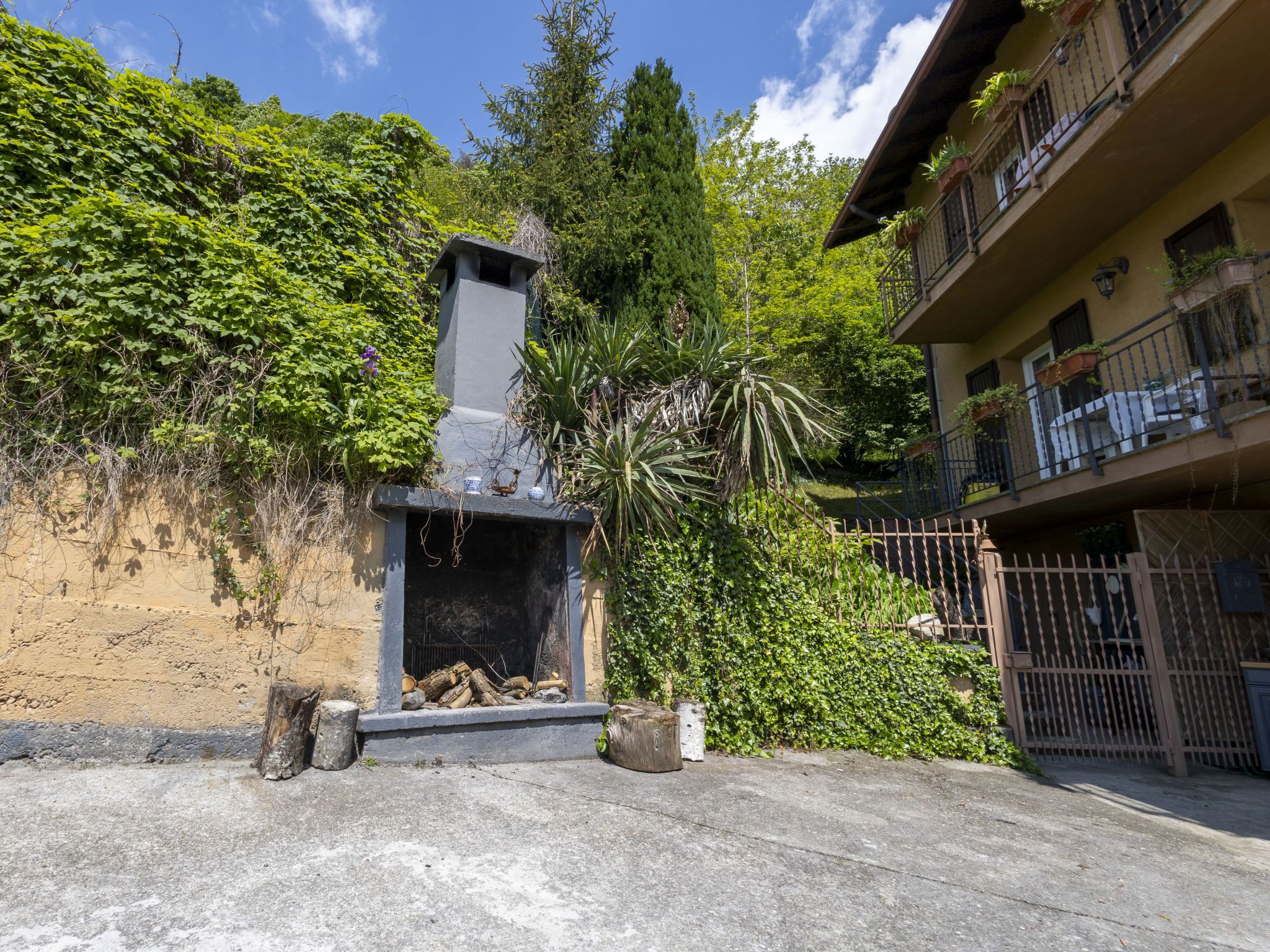 A courtyard with a stone fireplace, surrounded by lush greenery and a building with balconies.