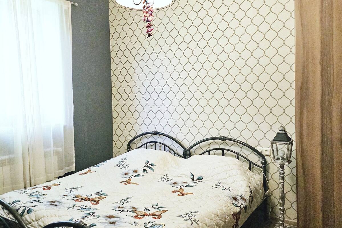 A bedroom with a bed, a hanging lamp, a patterned rug, and a window with curtains.