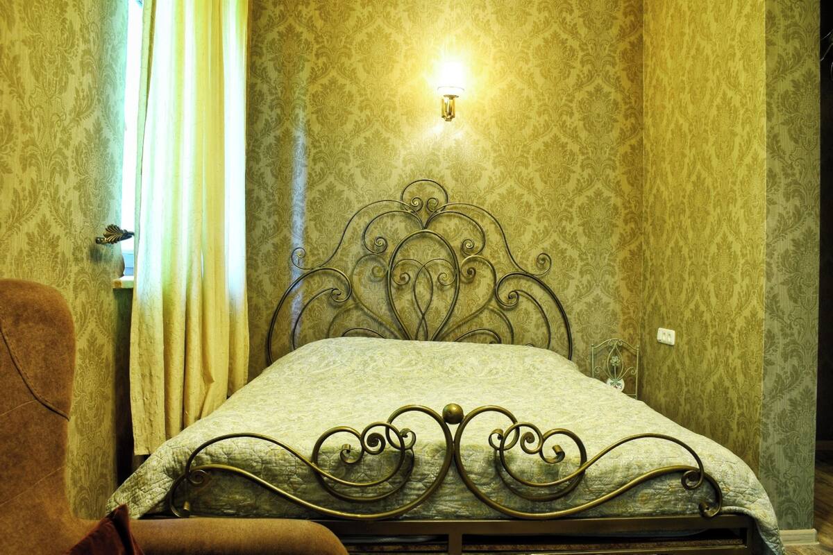 A room with a bed, curtains, a wall-mounted light, and a patterned wallpaper.