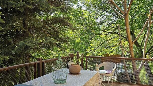 Une terrasse extérieure avec une table dressée pour deux personnes, entourée de chaises, d’une clôture en bois et d’arbres.
