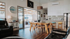 Un salon moderne avec un canapé en cuir noir, une table à manger en bois avec des chaises, et une grande fenêtre donnant sur l’extérieur.