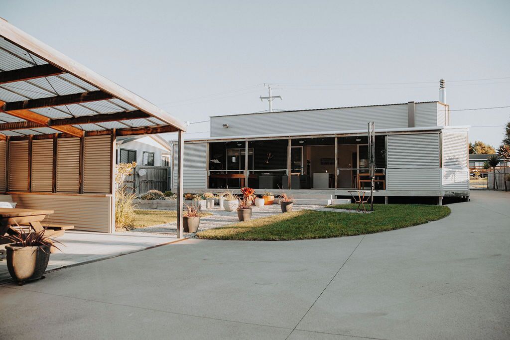 A modern building with a large glass facade, a covered outdoor area with seating, and a well-maintained lawn.
