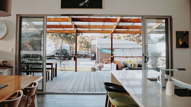 Une cuisine moderne dotée d’un grand îlot central, de portes-fenêtres coulissantes donnant sur une terrasse extérieure et d’un coin repas avec des chaises.