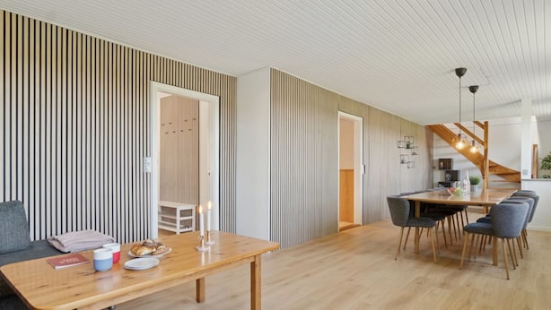A modern interior with a wooden dining table, grey chairs, and a staircase leading to an upper level.
