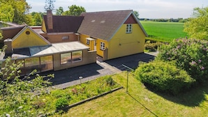 A yellow house with a sloped roof, a visible chimney, and a small attached structure with a glass enclosure.