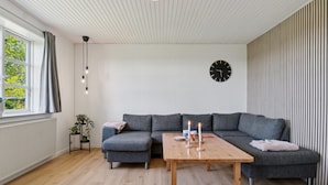 A modern living room with a grey sectional sofa, a wooden coffee table with candles, and a black clock on the wall.