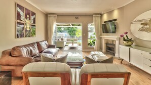 Una sala de estar con un sofá de cuero marrón, sillones blancos, una mesa de centro y un televisor sobre un mueble blanco.