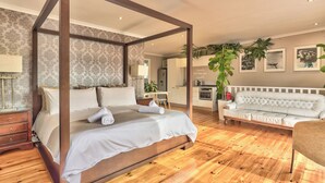 Una cama con dosel sobre un marco de madera, un sofá tapizado en blanco y un piso de madera.