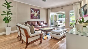 Amplia sala de estar con un sofá de cuero marrón, sillones blancos, una mesa de centro de vidrio y una planta en maceta.