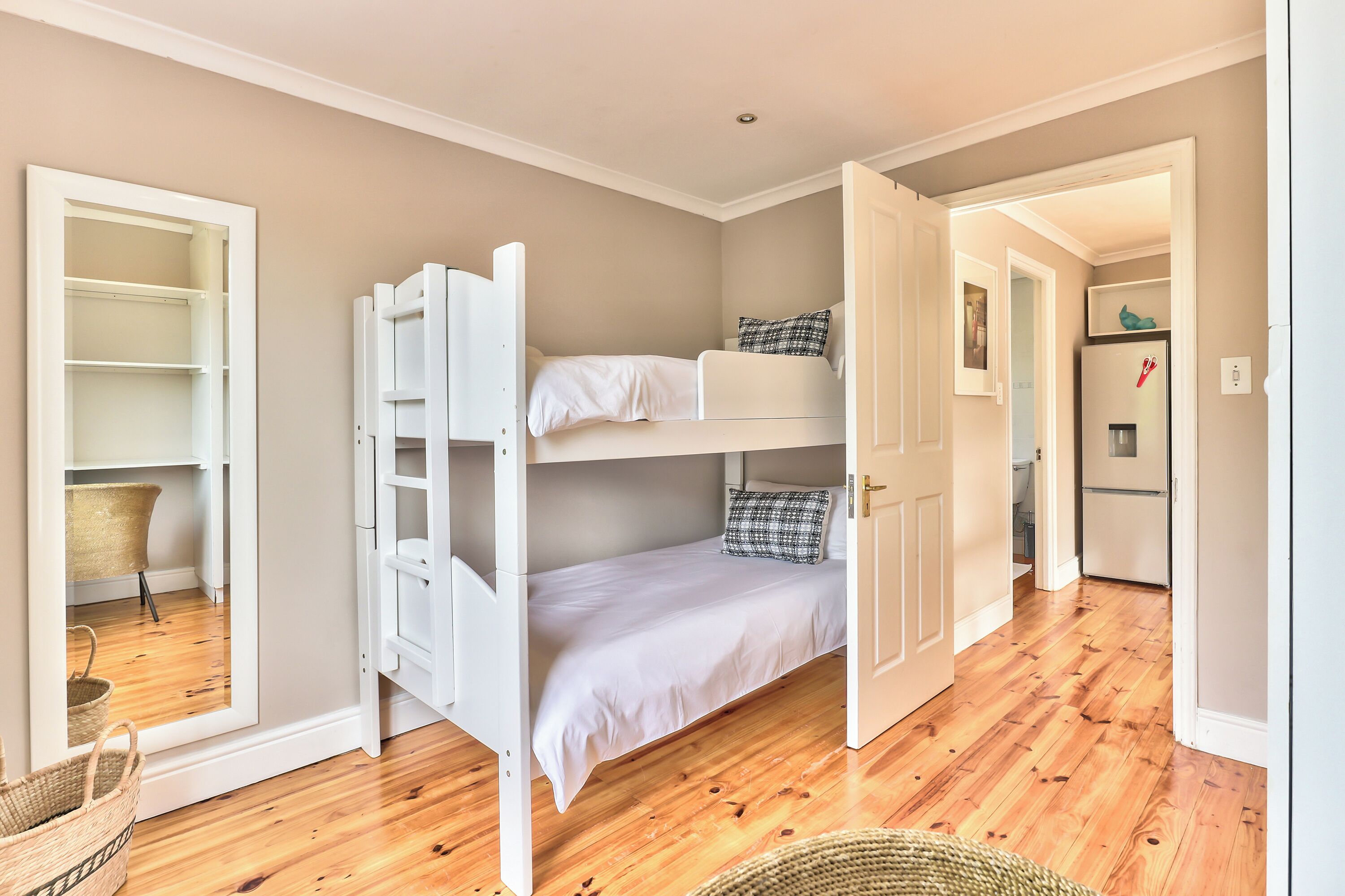 Una cama individual en un dormitorio con suelo de madera, un armario blanco y una pequeña cocina.