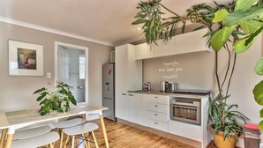 Una cocina moderna con armarios blancos, una mesa de comedor de madera con sillas y plantas en macetas.