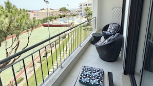 Un balcon avec vue sur une piscine et un court de tennis, aménagé avec un canapé et des coussins.