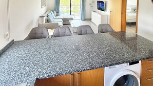 Une cuisine moderne dotée de plans de travail en granit, d’un lave-linge encastré et d’un coin repas avec un canapé et des fauteuils.
