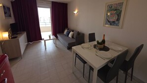 Un salon moderne comprenant un coin repas, un canapé, un téléviseur et un balcon agrémenté de rideaux.