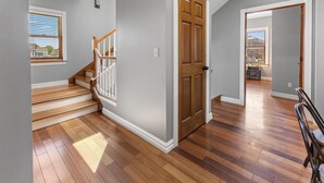 Una escalera con escalones de madera y barandillas blancas, una puerta de madera y vista a una habitación con una ventana y una mesa.