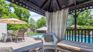 A covered outdoor seating area with a pool, wicker furniture, and a pergola.