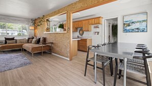A modern kitchen with wooden cabinets, a dining area with a glass table, and a cozy seating area with a sofa.