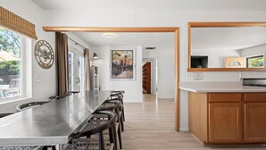 A modern kitchen with a long island, bar stools, and a large window.