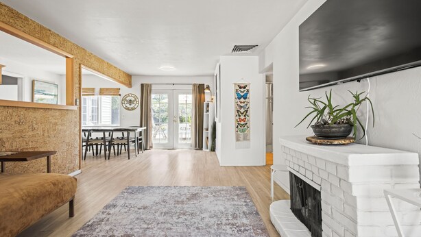 A modern living room with a fireplace, a large TV, and a dining area with natural light.