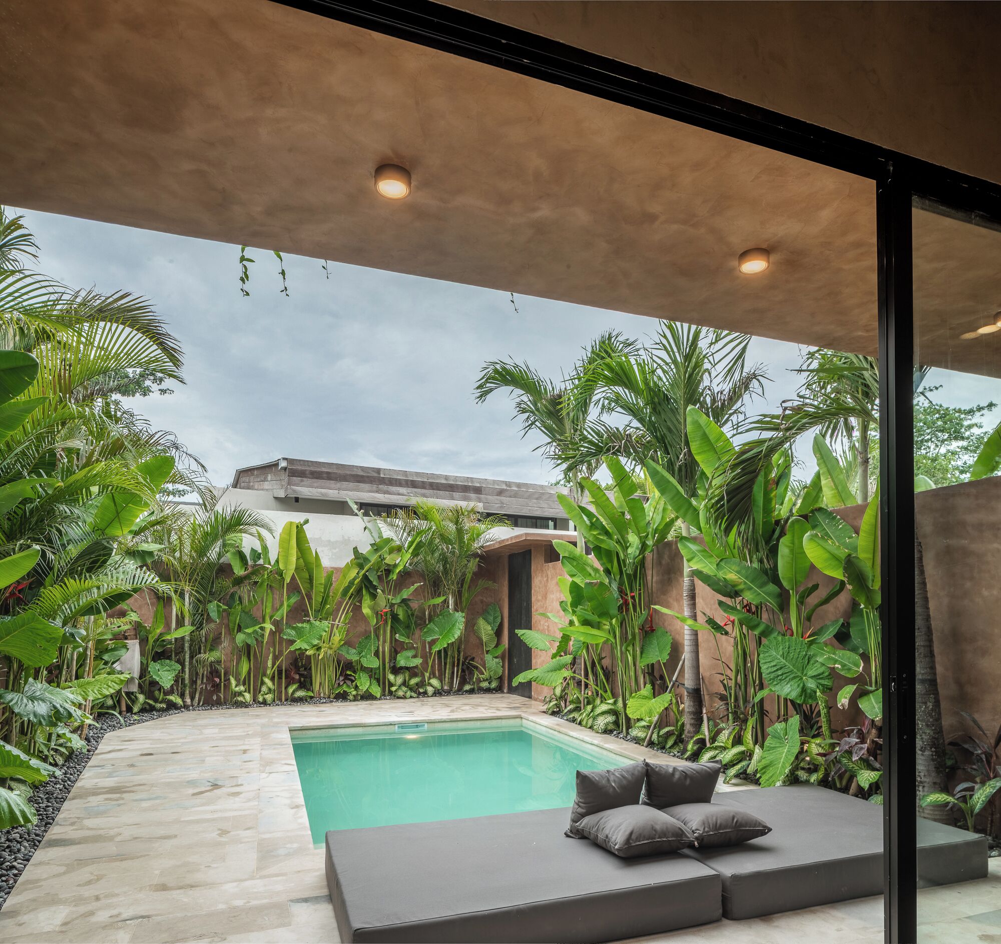 A modern outdoor pool area with a built-in seating area and lush tropical plants.