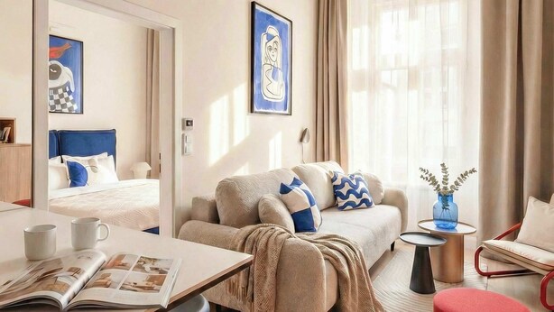 A modern living room with a sofa, coffee table, and ottoman, a dining area with a table and chairs, and a large mirror. - TurnKey | Wenceslas square Two Level Apartment III (Praha 1)