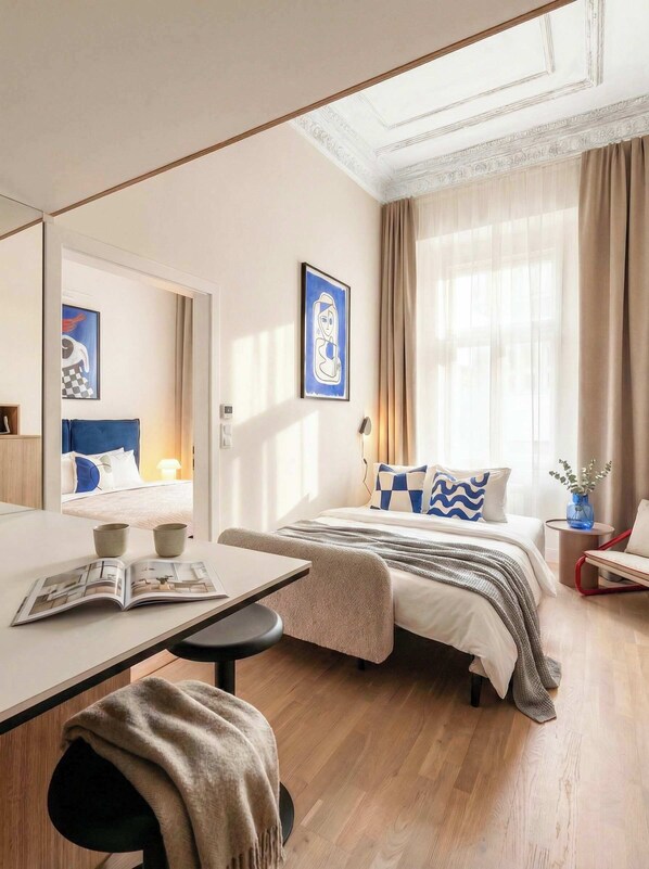 A hotel room with a bed, a desk, a chair, a mirror, and a window with curtains. - TurnKey | Wenceslas square Two Level Apartment III (Praha 1)