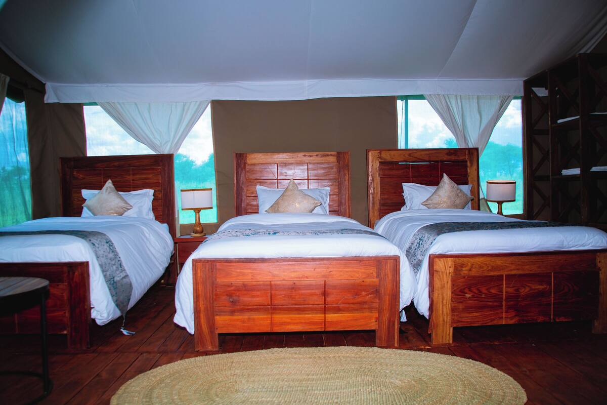 Une chambre avec trois lits en bois, chacun doté d’une tête de lit en bois, de draps blancs et d’une petite table de chevet.