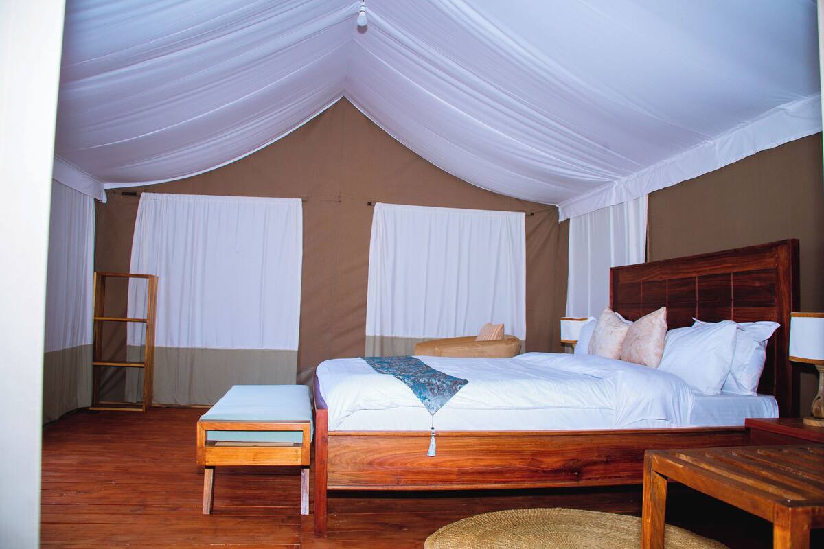 Une chambre spacieuse avec un grand lit, des meubles en bois et des rideaux blancs.