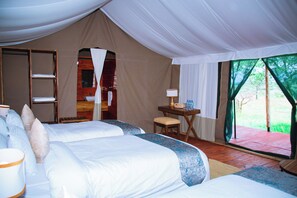 Habitación tipo tienda con dos camas, una mesita con lámpara y vistas al exterior con vegetación.