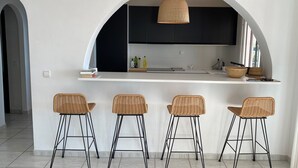 A modern kitchen with a white island, black cabinets, and three wicker bar stools. - Villa Lantana - Private pool and sea views (Sayalonga)