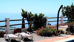A poolside area with two lounge chairs, a small garden with flowers, and a view of the sea. - Villa Lantana - Private pool and sea views (Sayalonga)