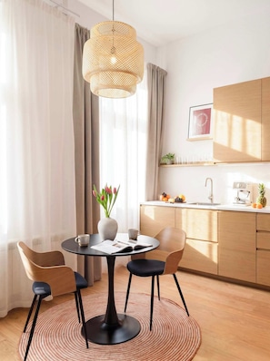 A modern dining area with a round table, chairs, a vase with flowers, and a hanging light fixture. - TurnKey | Vinohrady Modern Studio with Balcony II (Prague 3)