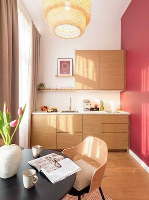 A modern kitchen with wooden cabinets, a dining area with a table and chairs, and a hanging light fixture. - TurnKey | Vinohrady Modern Studio with Balcony II (Prague 3)