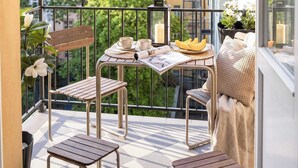 Ein Balkon mit einem Tisch für zwei Personen, Stühlen, einer kleinen Pflanze und Blick auf die Stadtlandschaft.