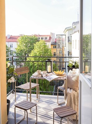 A balcony with a table set for two, chairs, a small plant, and a view of the cityscape. - TurnKey | Vinohrady Modern Studio with Balcony II (Prague 3)
