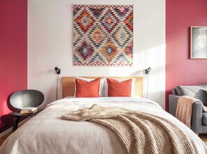 Een slaapkamer met een bed, kussens, een deken, een wanddecoratie en een stoel.