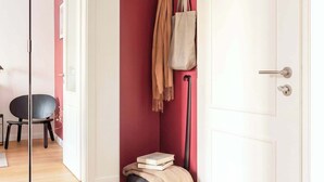 Ein Zimmer mit einer weißen Tür, einer roten Wand, einer schwarzen Stehlampe, einem schwarzen Sessel und einem kleinen Tisch mit Büchern und einer Decke.