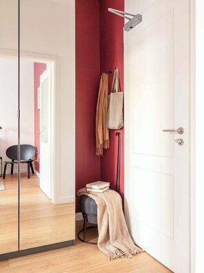 Ein Zimmer mit einer weißen Tür, einer roten Wand, einer schwarzen Stehlampe, einem schwarzen Sessel und einem kleinen Tisch mit Büchern und einer Decke.