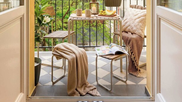 Un balcon avec une table, des chaises et une vue sur un arbre et des immeubles.