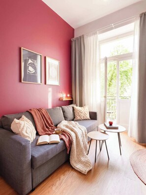 Un salon avec un canapé gris, une petite table ronde et une fenêtre avec des rideaux.