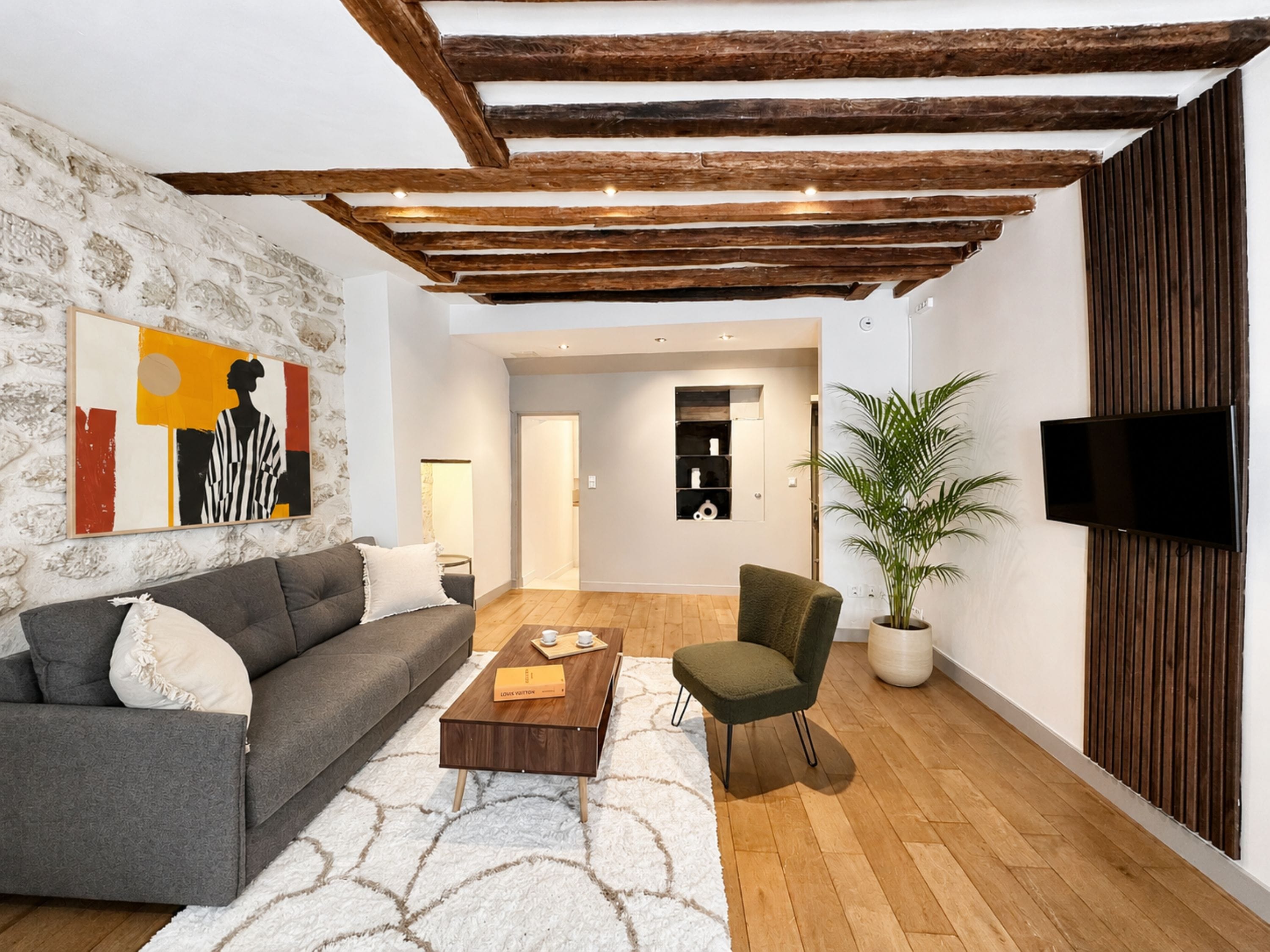 Ein modernes Wohnzimmer mit Steinwand, grauem Sofa, Holztisch, grünem Sessel und einem flachbildfernseher, der an einer Holzplatte angebracht ist.
