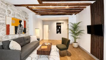 Una sala de estar moderna con pared de piedra, sofá gris, mesa de centro de madera, sillón verde y televisor de pantalla plana montado en un panel de madera.