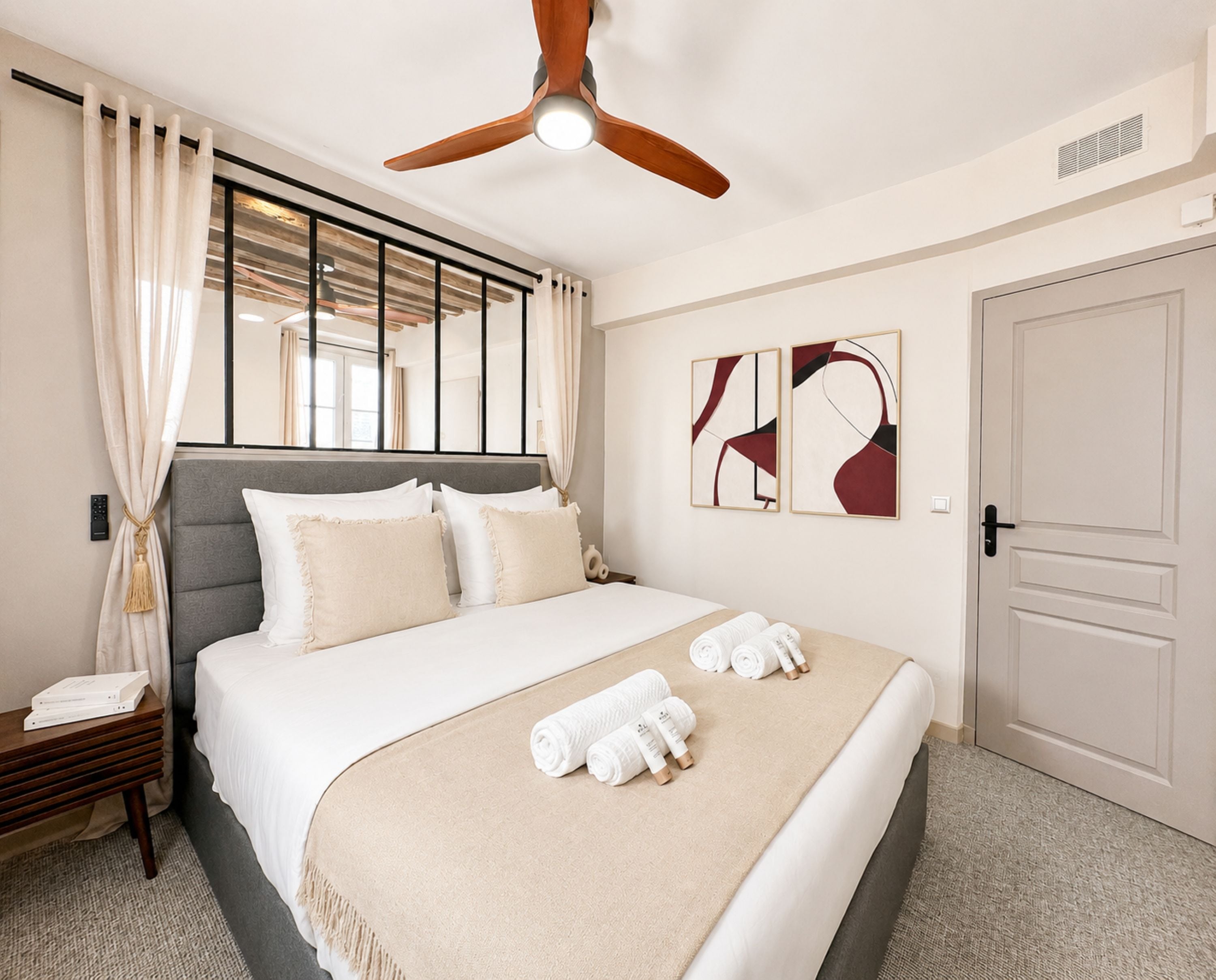 A hotel room with a bed, a ceiling fan, artwork on the wall, and a door.