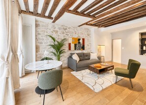 A modern living room with a stone wall, a round table, a sofa, and two chairs. - 1550 Nazareth (Paris)